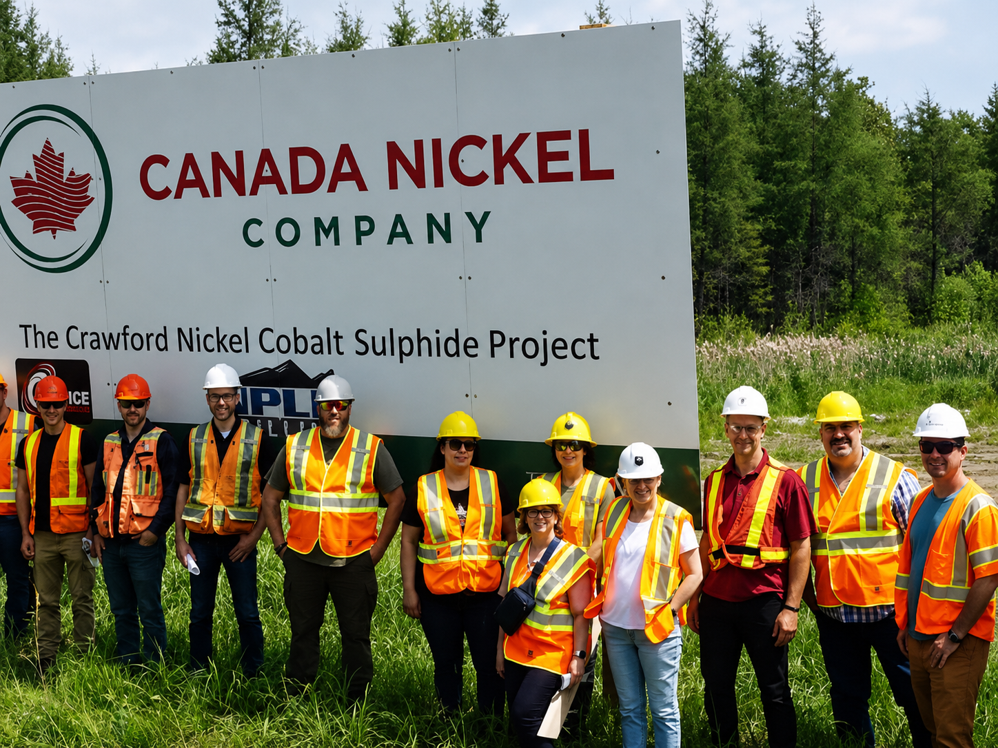 Un groupe de personnes portant des casques et des gilets de sécurité pose devant le panneau du projet Crawford de Canada Nickel.